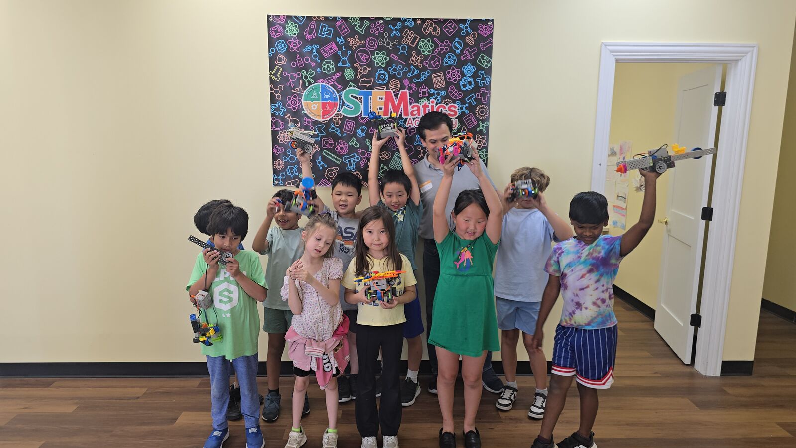 Camp students holding up the robots they built in front of the STEMatics Academy banner