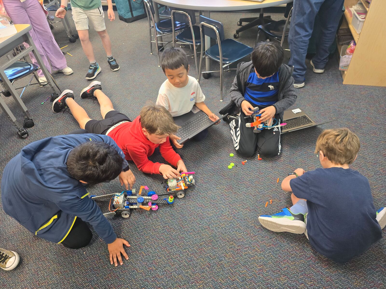 Students testing and adjusting robots on a classroom floor