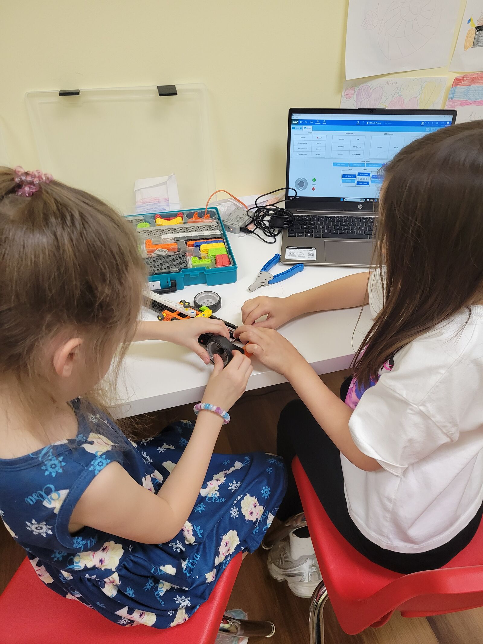 Two students assembling a robot beside a laptop running VEXcode